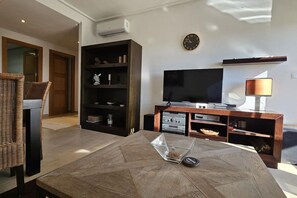 A living room with a flat-screen TV, a wooden entertainment unit, a glass coffee table, and a wicker chair. - Beautiful apartment PA923LT, Casa Gironi (Murcia)