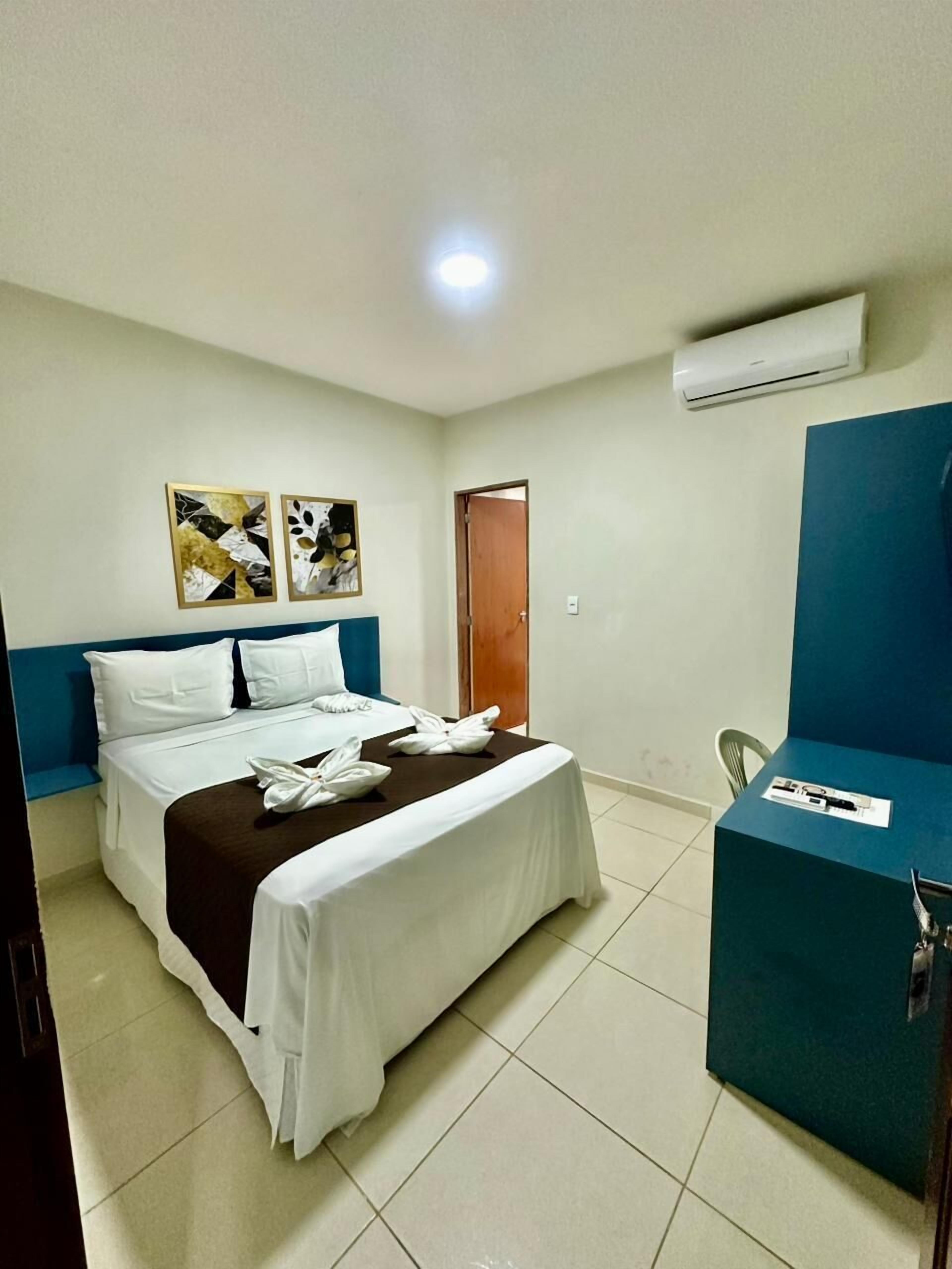 A hotel room with a bed, a desk, and an air conditioning unit.