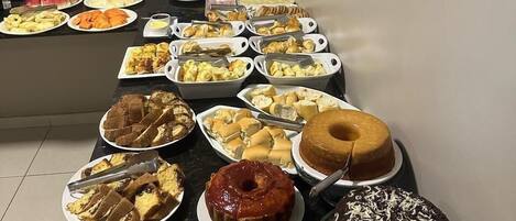 Una mesa de buffet con diversas opciones de comida, incluyendo pasteles, bollería y frutas.