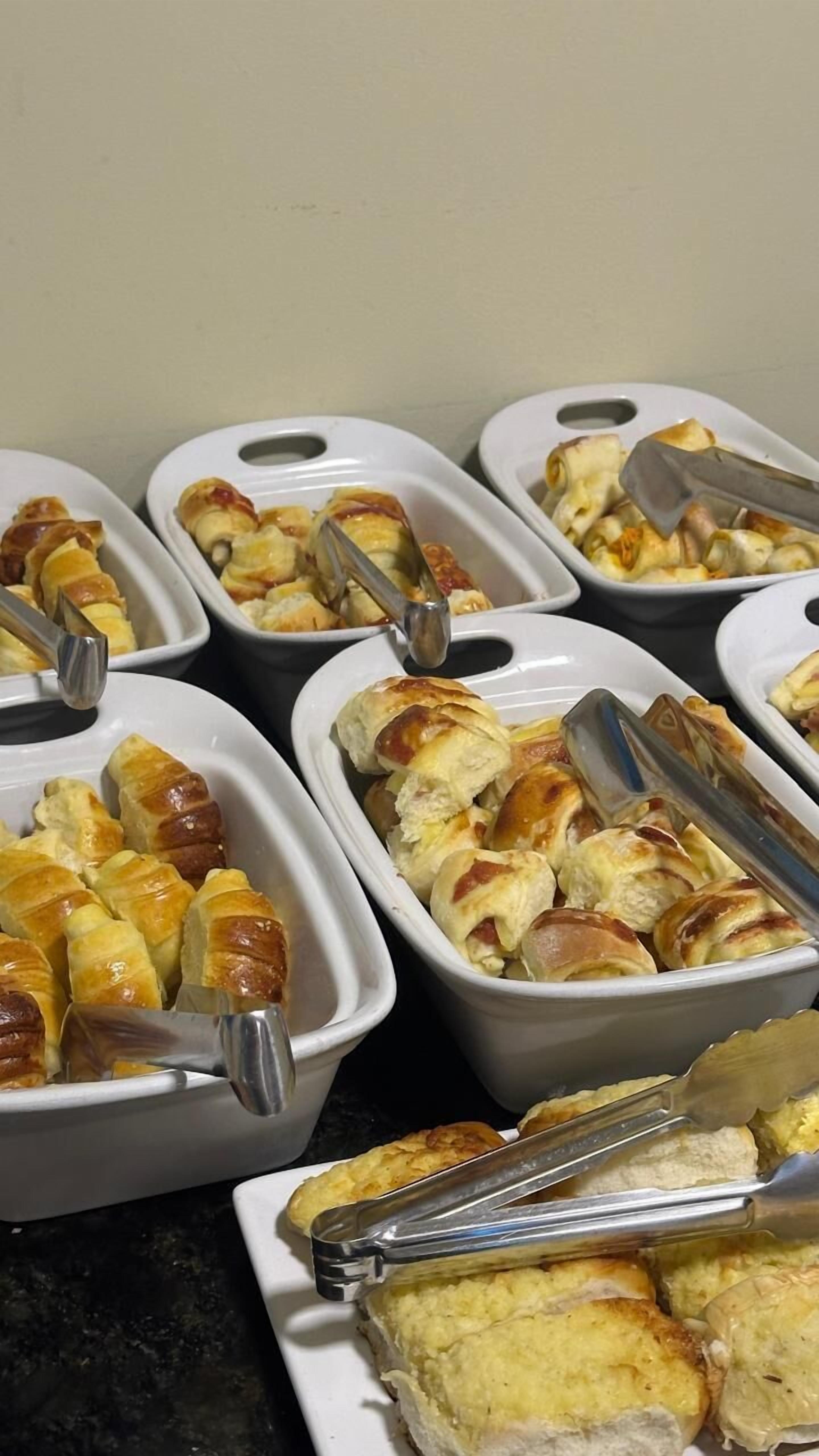 Multiple white serving dishes with golden-brown pastries and tongs.