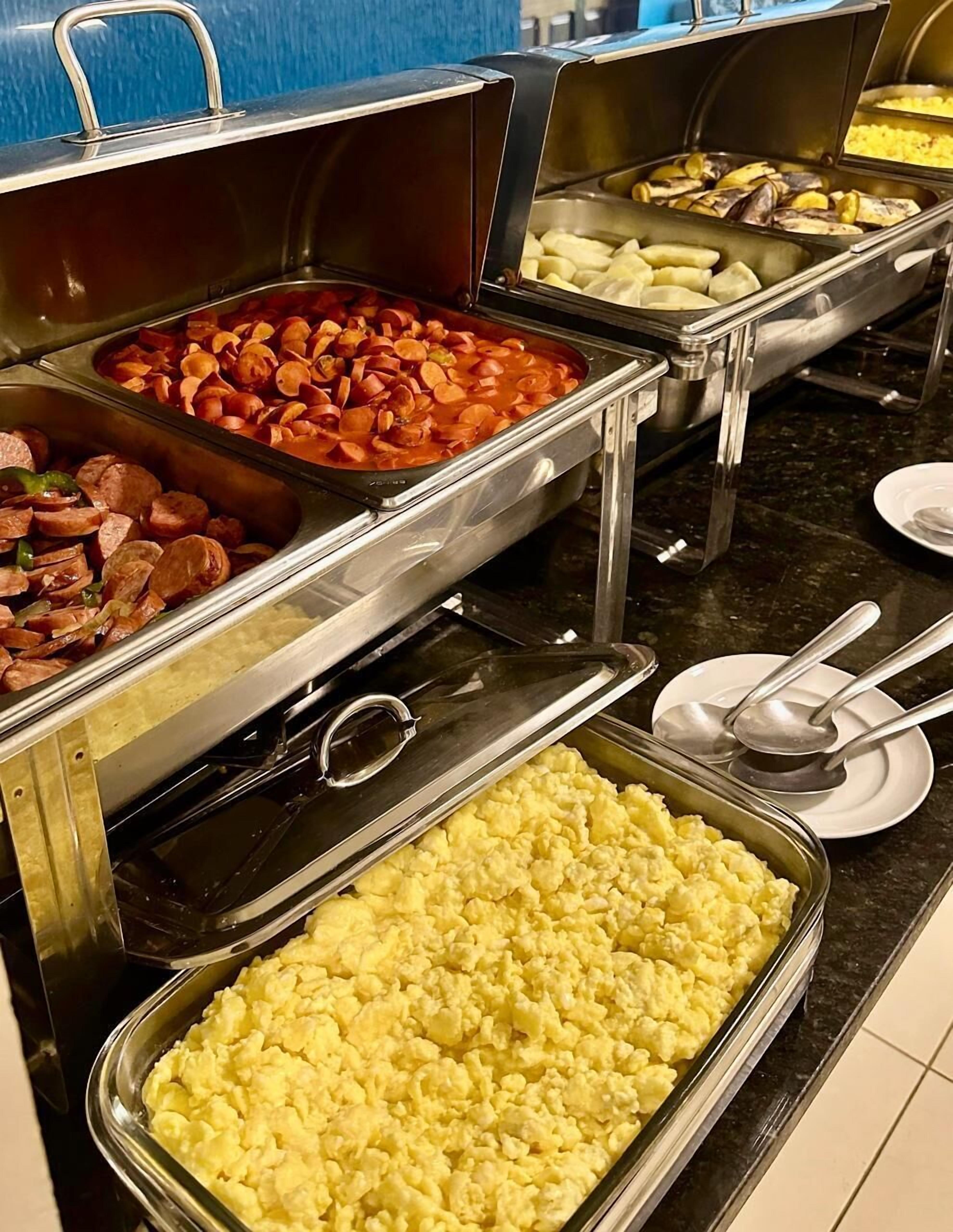 A buffet with various food options including sausages, potatoes, and scrambled eggs.