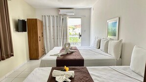 A hotel room with two beds, a wooden wardrobe, a TV, and a view of the outdoors. - Pousada Caribe Brasileiro (Maragogi)