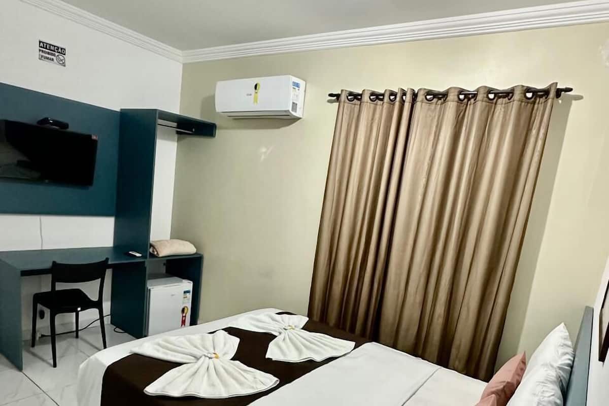Ein Hotelzimmer mit Bett, Schreibtisch, Stuhl, Klimaanlage und Vorhängen.