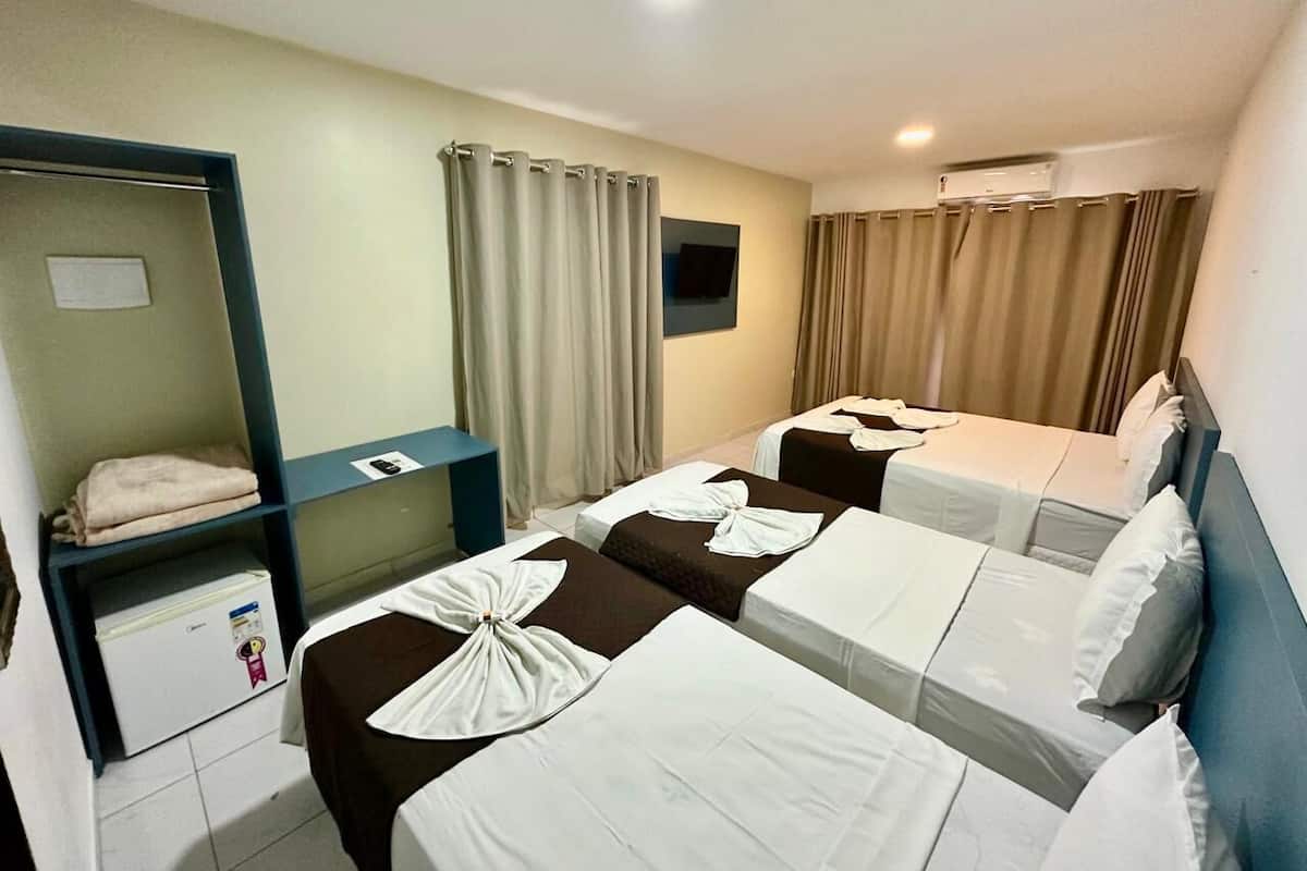 Ein Hotelzimmer mit drei Betten, einem kleinen Fernseher, einem Kühlschrank und einem Regal mit Handtüchern.