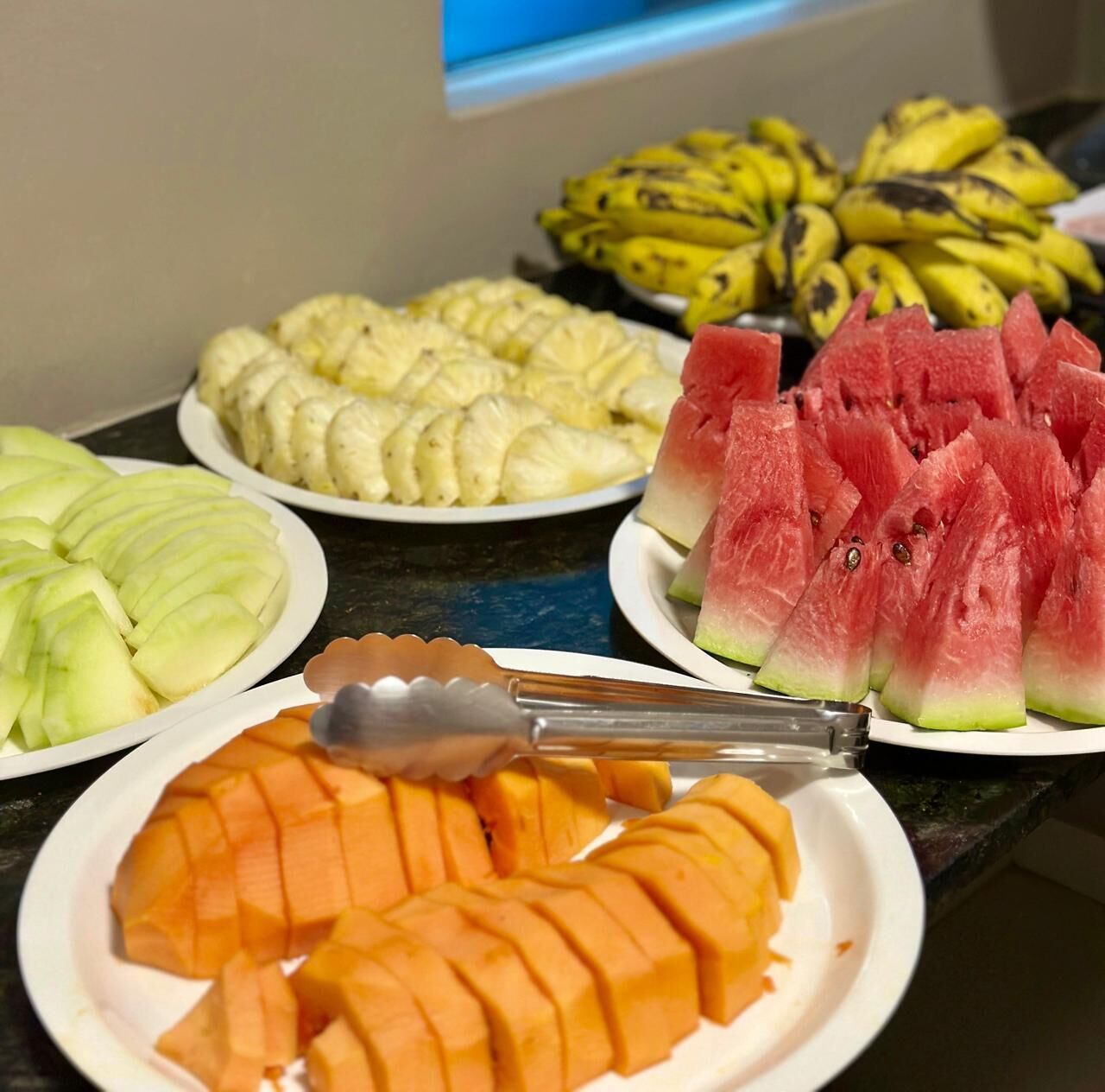Een buffet met verschillende soorten fruit, zoals appels, bananen, watermeloen en mango's.