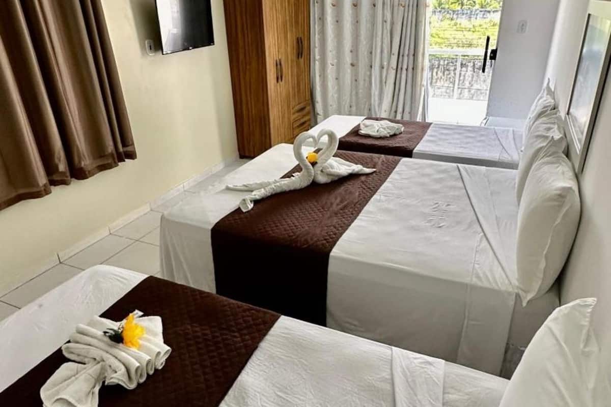Ein Hotelzimmer mit zwei Betten, jeweils mit einer braunen Steudecke und weißen Bettwäsche. Handtücher und eine kleine gelbe Blume liegen auf den Betten.