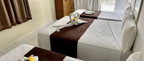 A hotel room with two beds, each with a brown quilt and white linens. There are towels and a small yellow flower on the beds.