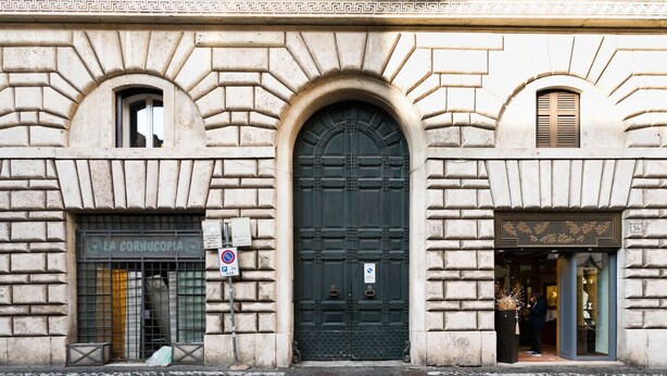 Une façade d’immeuble avec une grande porte centrale, un magasin à gauche et une fenêtre à droite.