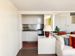A modern kitchen with white cabinets, a stove, and a sink. There is a white sofa with orange and gray cushions in the living area. - Penthouse with Terrace near Pantheon (Roma)