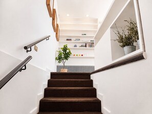 Un escalier avec une rampe, une plante en pot et une bibliothèque en arrière-plan.