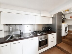 Une cuisine moderne avec des meubles blancs, un évier en acier inoxydable, une cuisinière à gaz, un four et un lave-linge encastré.