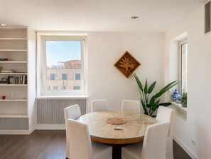 A modern dining area with a round table, white chairs, a radiator, a window with a view of buildings, and a decorative wooden piece on the wall. - Penthouse with a terrace near the Pantheon (Roma)