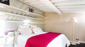 Une chambre à coucher avec un lit, une lampe de chevet, une fenêtre et un plafond avec des poutres apparentes.