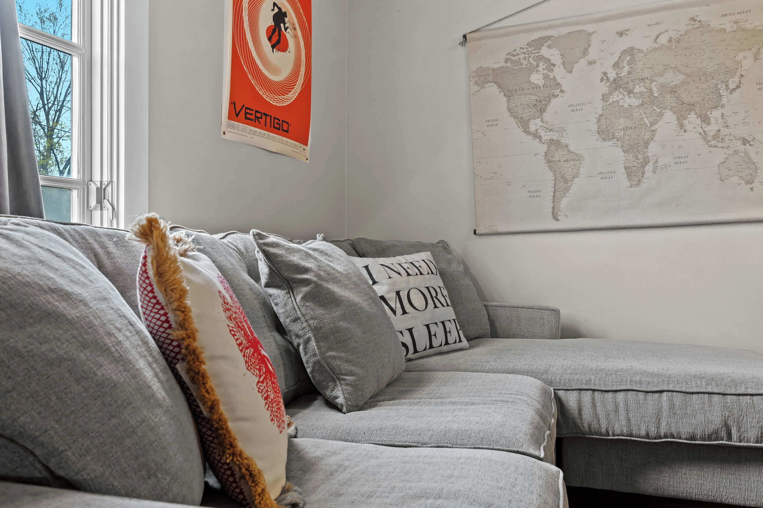 Ein graues Sofa mit Zierkissen, eine Weltkarte an der Wand und ein Plakat mit einer Tänzerin.