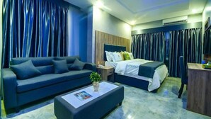 A modern hotel room with a sofa, a bed, a desk, and a coffee table. - Golden Grand Royale Hotel  (Lokoja)