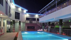 A swimming pool with a wooden deck and red LED lights, surrounded by a modern building with balconies and a covered walkway. - Golden Grand Royale Hotel  (Lokoja)