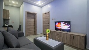 A modern living room with a grey sofa, a flat-screen TV, and wooden cabinets. - Golden Grand Royale Hotel  (Lokoja)