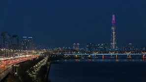 A nighttime cityscape with a prominent illuminated skyscraper, a busy bridge, and a river reflecting city lights. - Original Backpackers (Seoul)