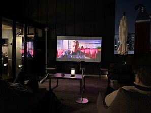 A dark room with a large screen displaying a movie, a small table with a lamp, and a few chairs. - Original Backpackers (Seoul)