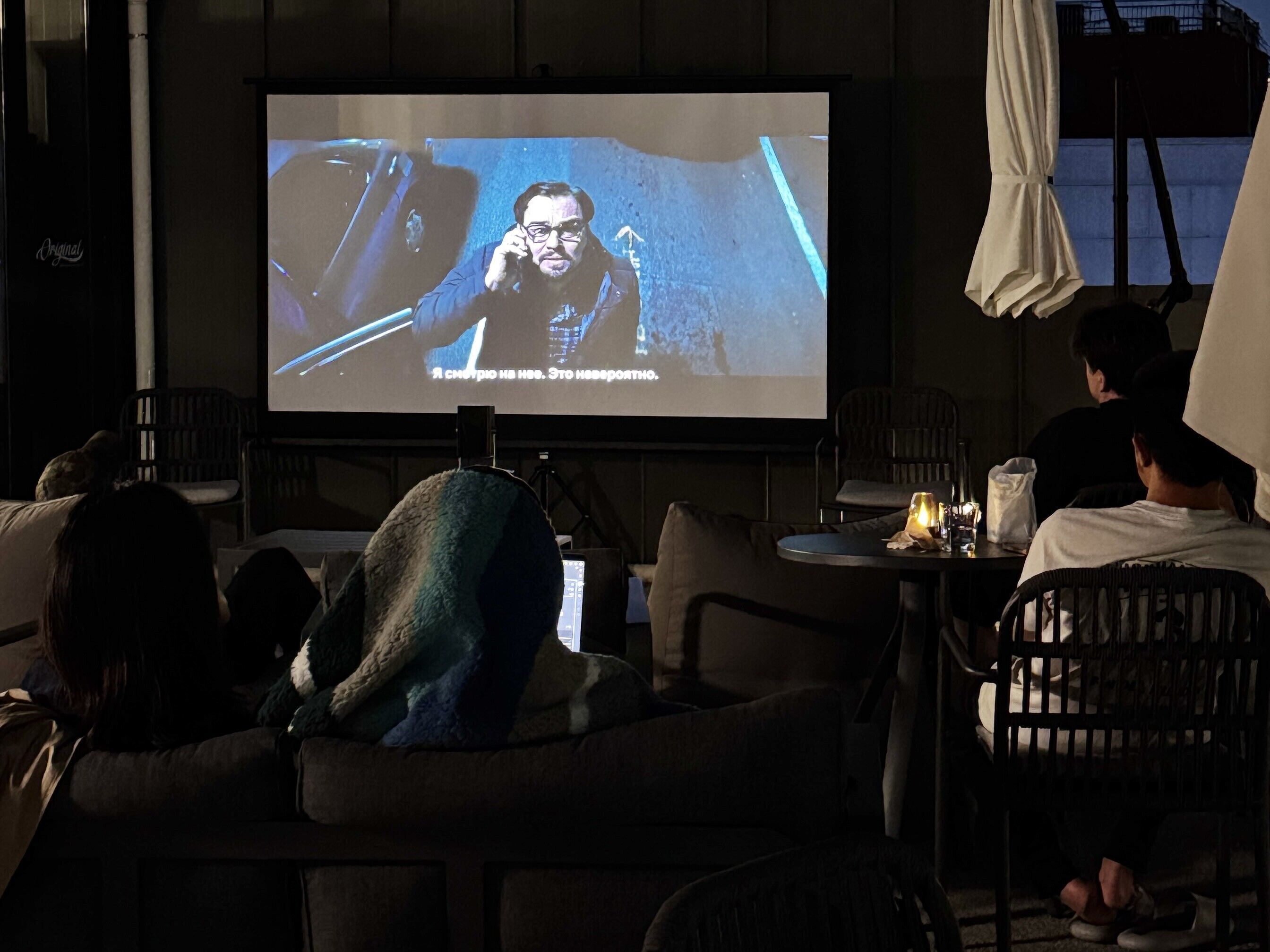 A room with a large screen displaying a movie, a sofa, and a table with a lamp.