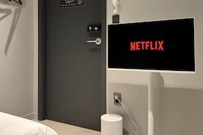 A room with a door, a wall-mounted television displaying the Netflix logo, and a white trash bin. - Original Backpackers (Seoul)