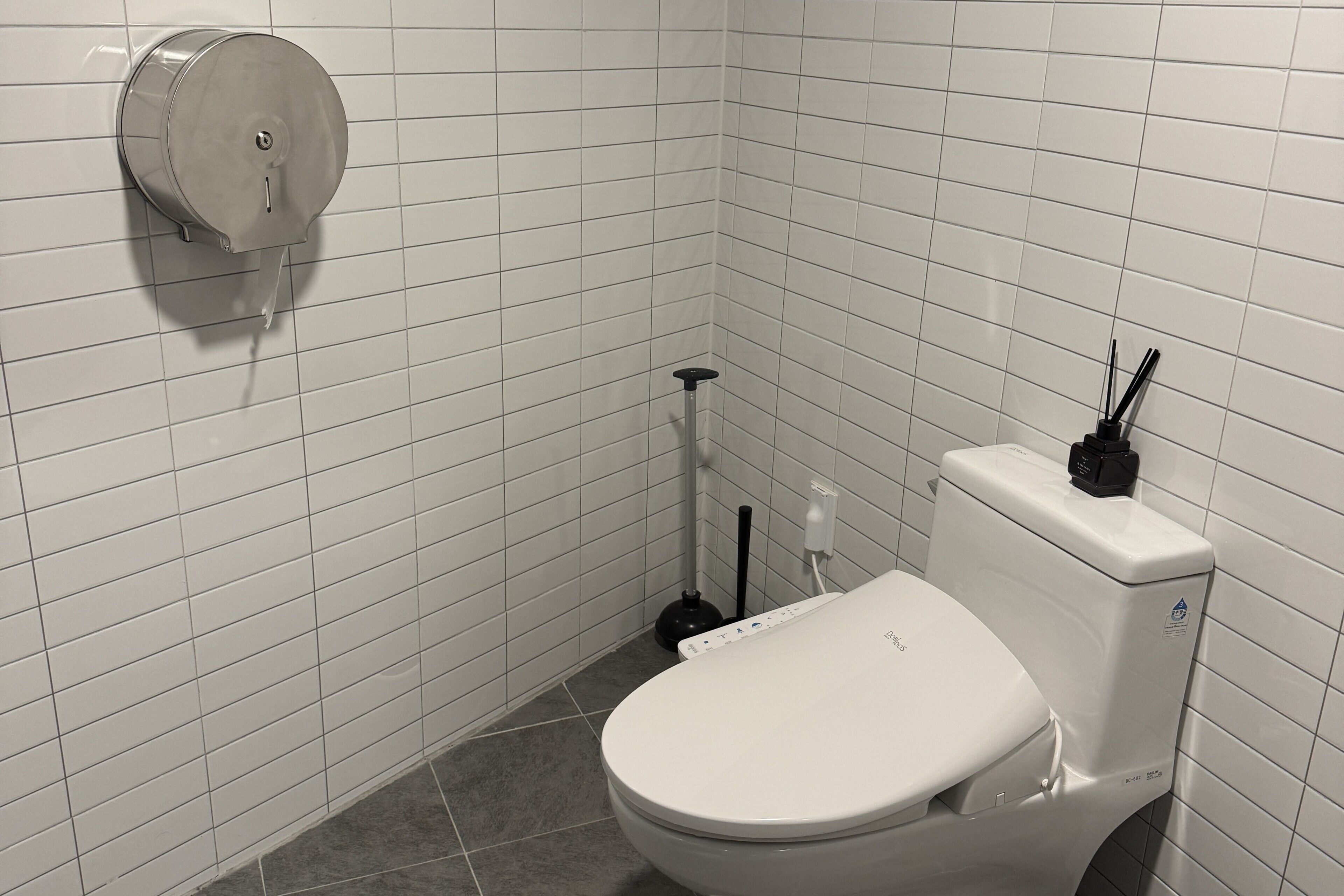A small, white-tiled bathroom with a toilet, a bidet, and a toilet paper holder.