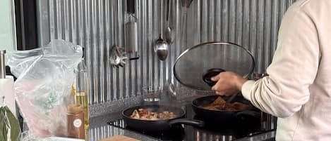 En person laver mad i et køkken med en komfur, gryder og en skærebræt med forberedte ingredienser.