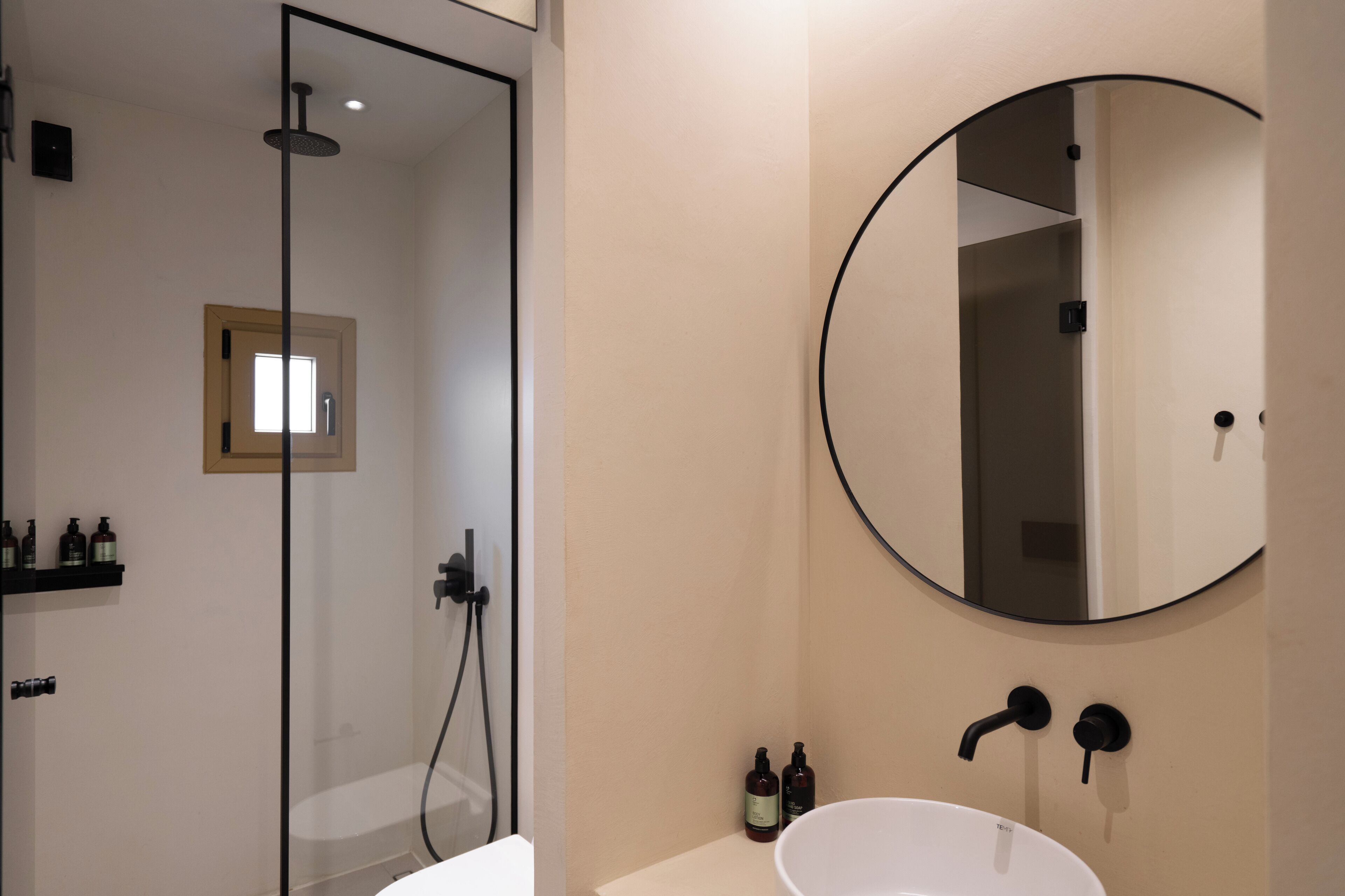 A modern bathroom with a glass shower enclosure, a round mirror, and a white sink.