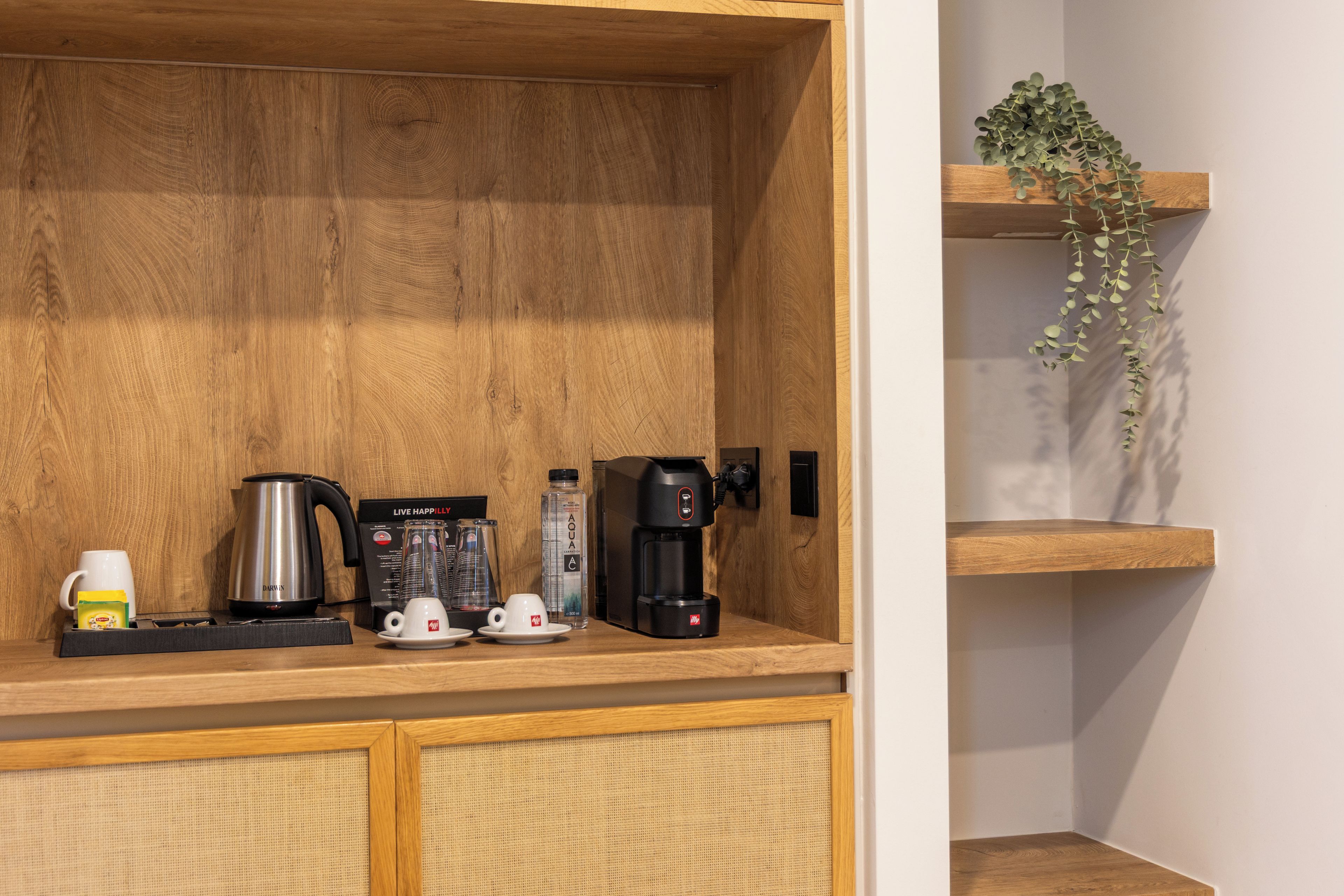 A wooden kitchen counter with a coffee maker, a kettle, a water bottle, and a cup.