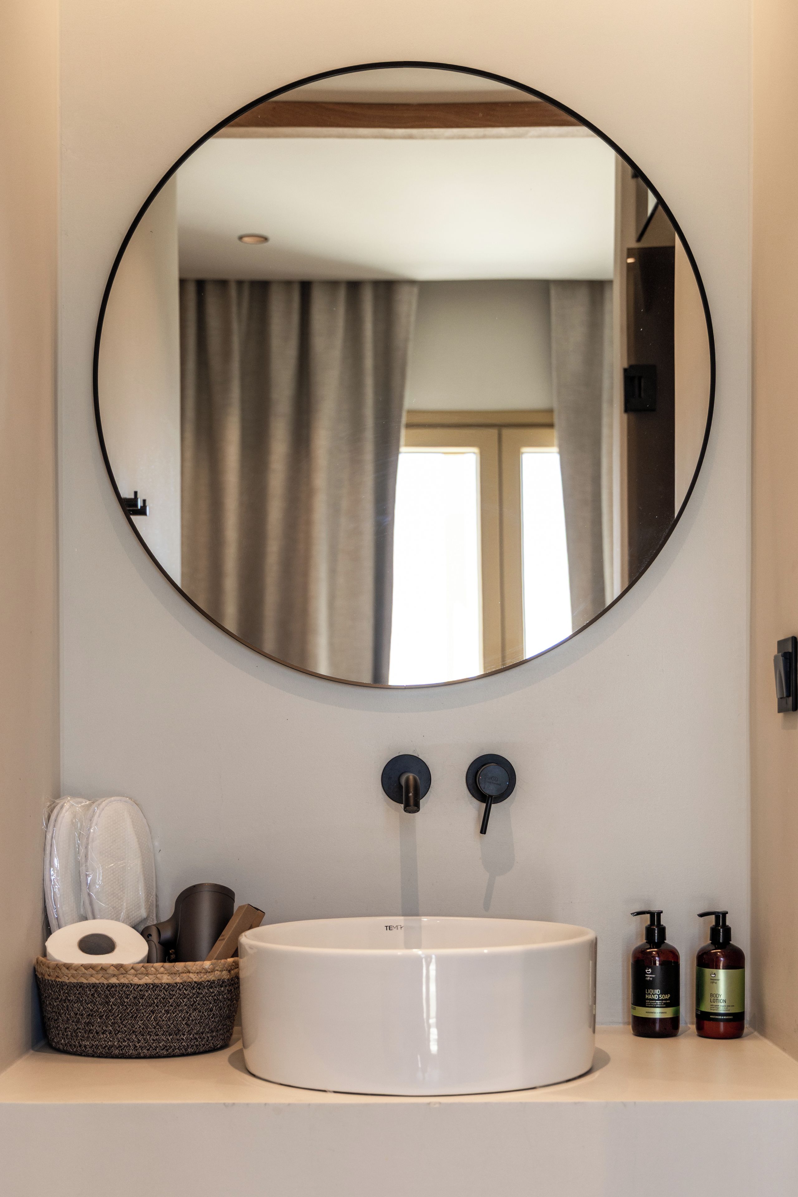 Een badkamer met een ronde spiegel, een witte wasbak en toiletartikelen.