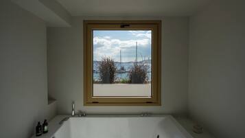 Une salle de bain dotée d’une grande fenêtre, d’une baignoire et d’une petite étagère où sont rangés les articles de toilette.