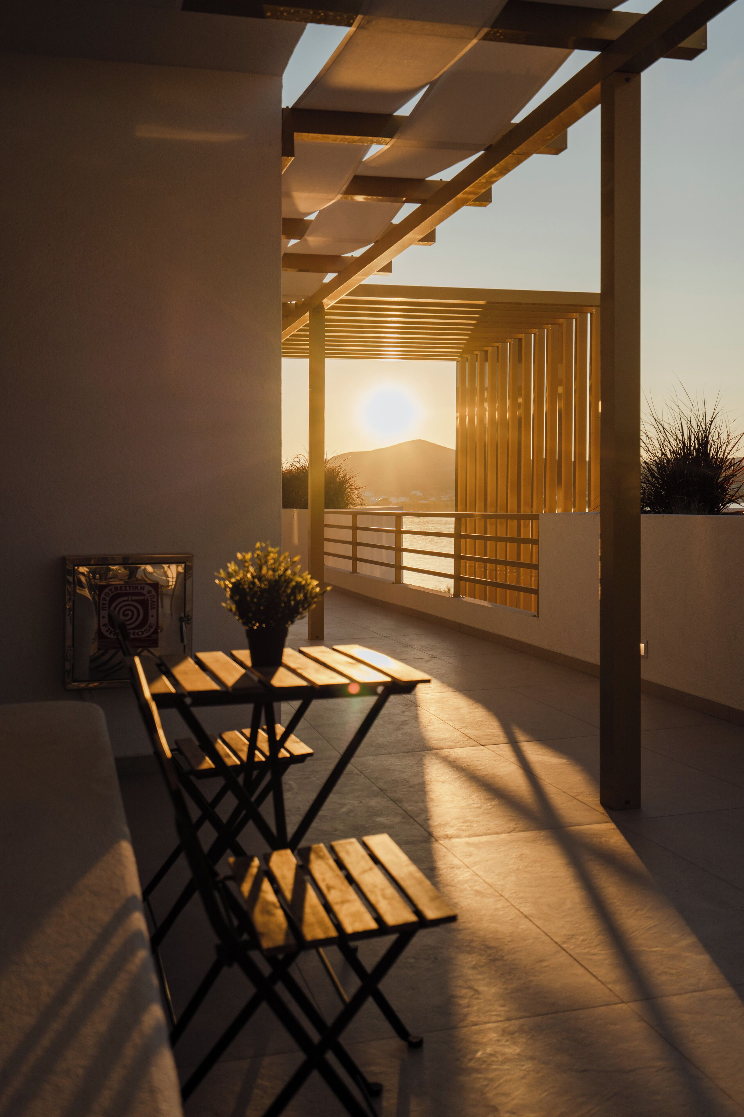 Eine moderne Terrasse im Freien mit einem Holztisch und Stühlen, einem Blumentopf und Blick auf den Sonnenuntergang über dem Wasser.
