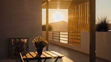 Eine moderne Terrasse im Freien mit einem Holztisch und Stühlen, einem Blumentopf und Blick auf den Sonnenuntergang über dem Wasser.