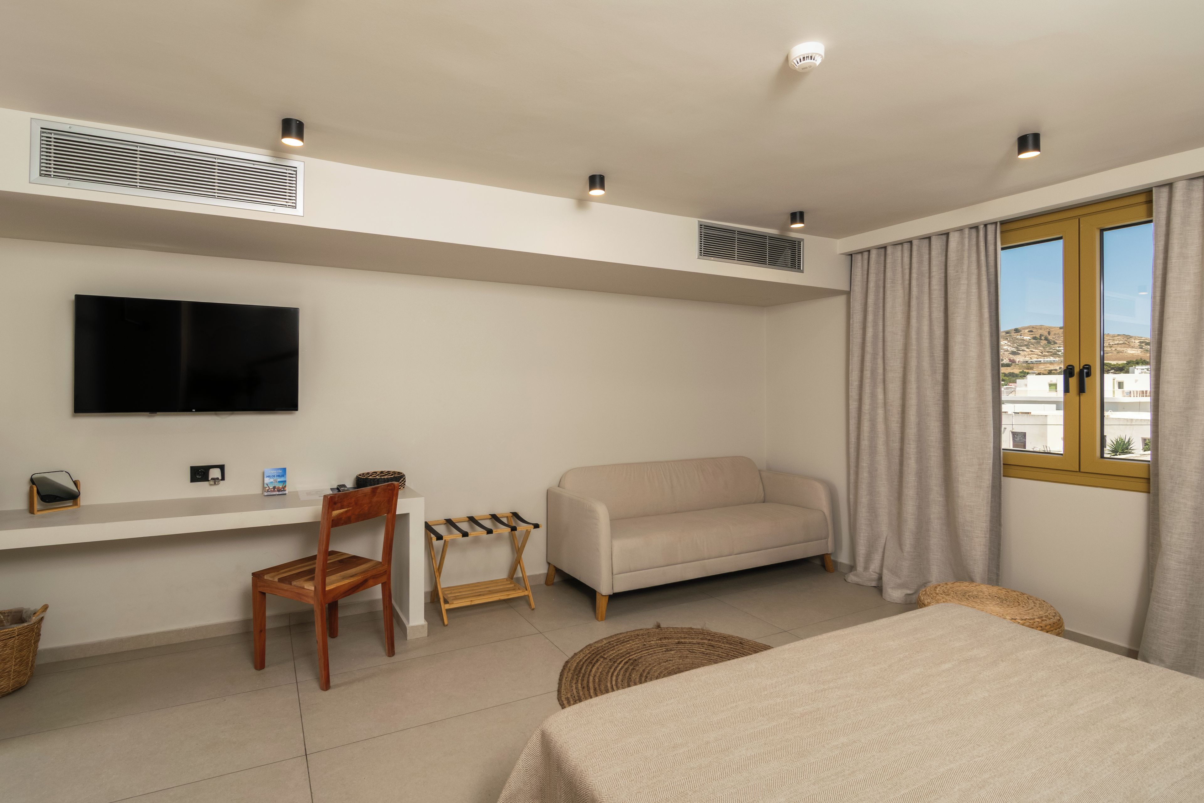 A hotel room with a bed, a sofa, a TV, a desk, and a window with curtains.