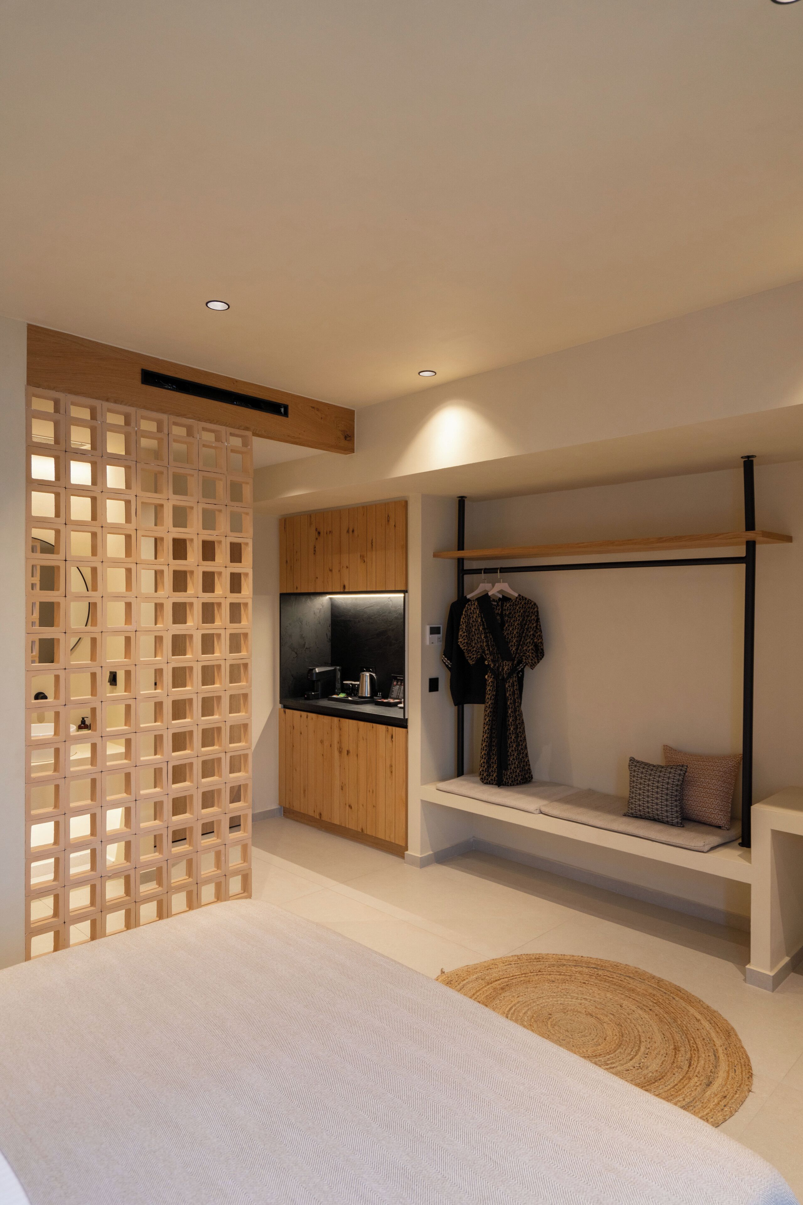 A modern bedroom with a built-in wardrobe, a small kitchenette, a hanging robe, and a bedside table.