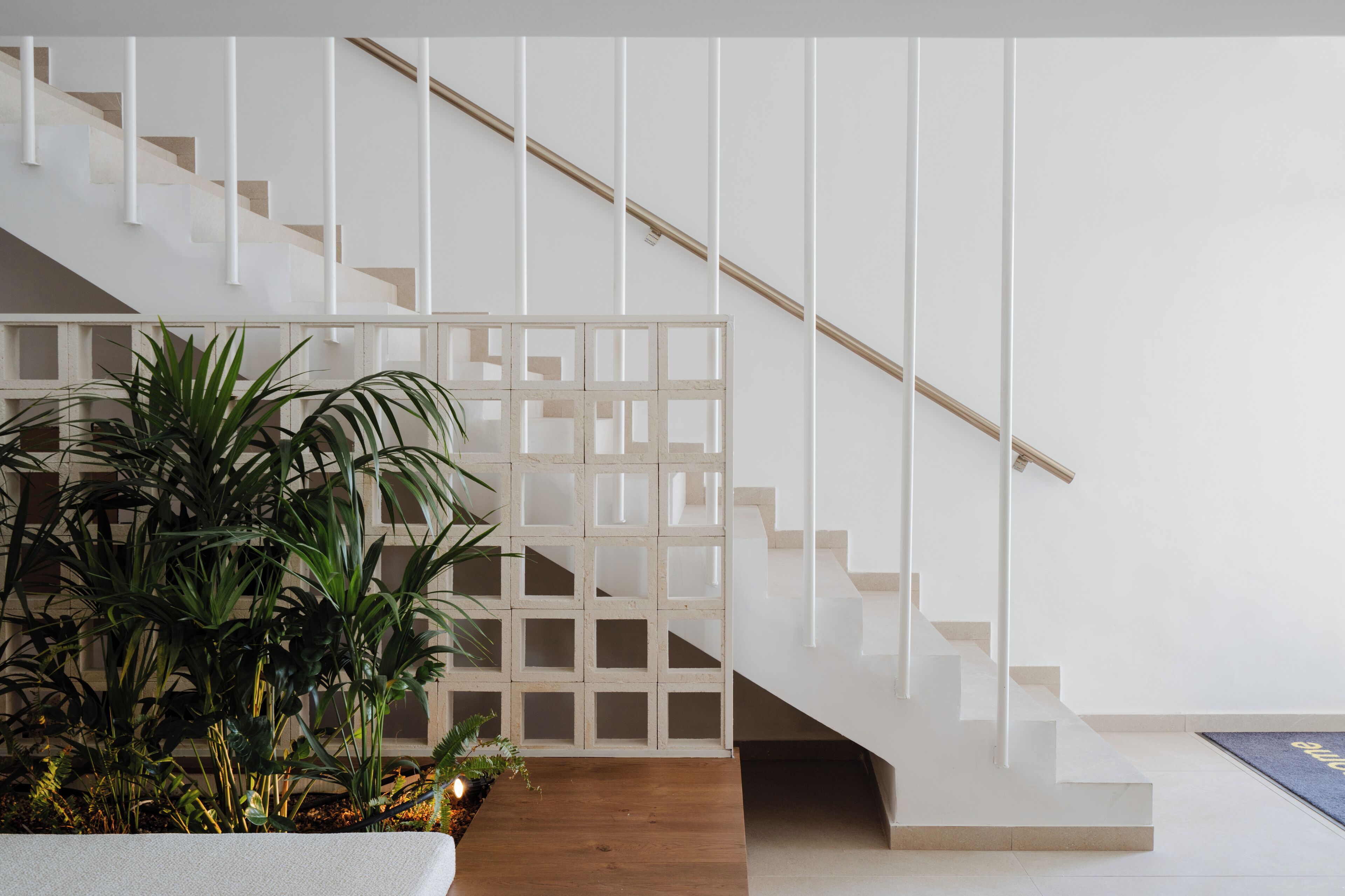 Una escalera con barandilla de madera y una baranda blanca, que lleva a un rellano con un tapete azul.
