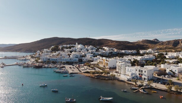 Une ville côtière aux bâtiments blancs, un port de plaisance avec des bateaux et un paysage vallonné en arrière-plan.