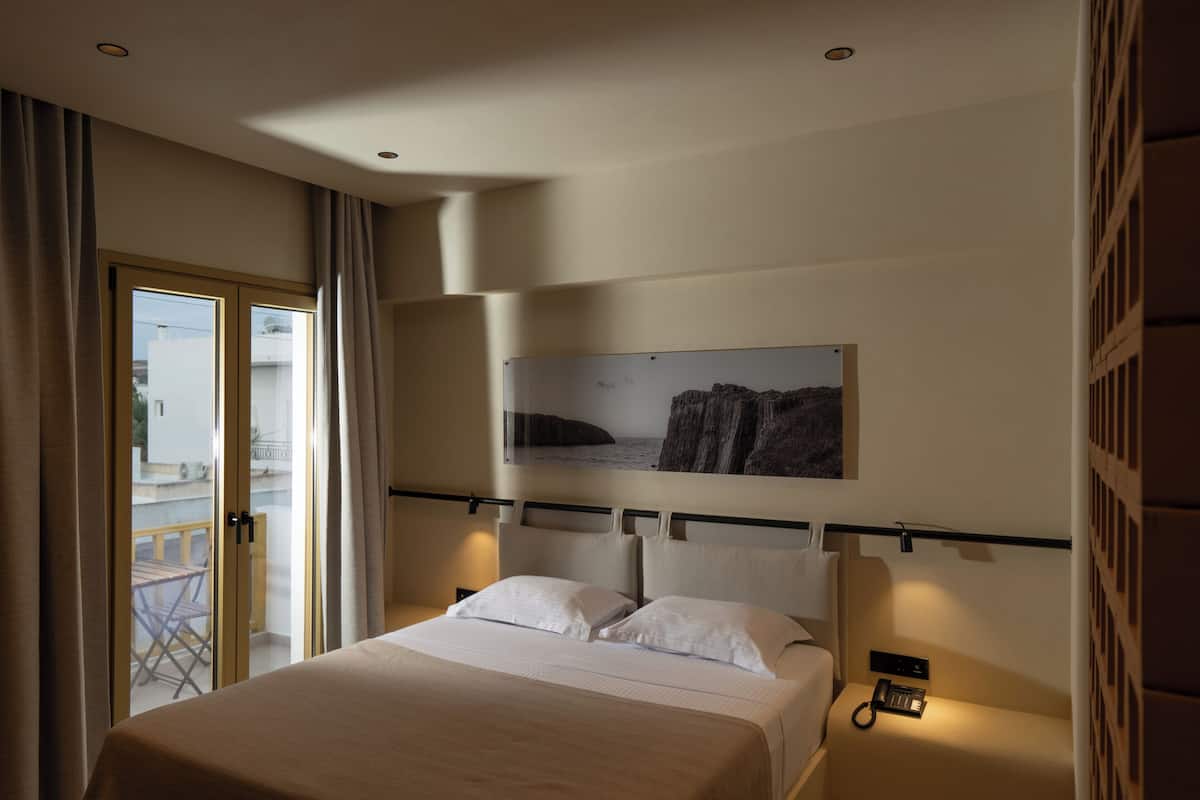 Et hotelværelse med seng, natbord, telefon og et vindue med gardiner.