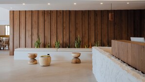 Un espace d’accueil moderne avec un mur revêtu de panneaux en bois, un comptoir d’accueil blanc et trois tabourets en bois.