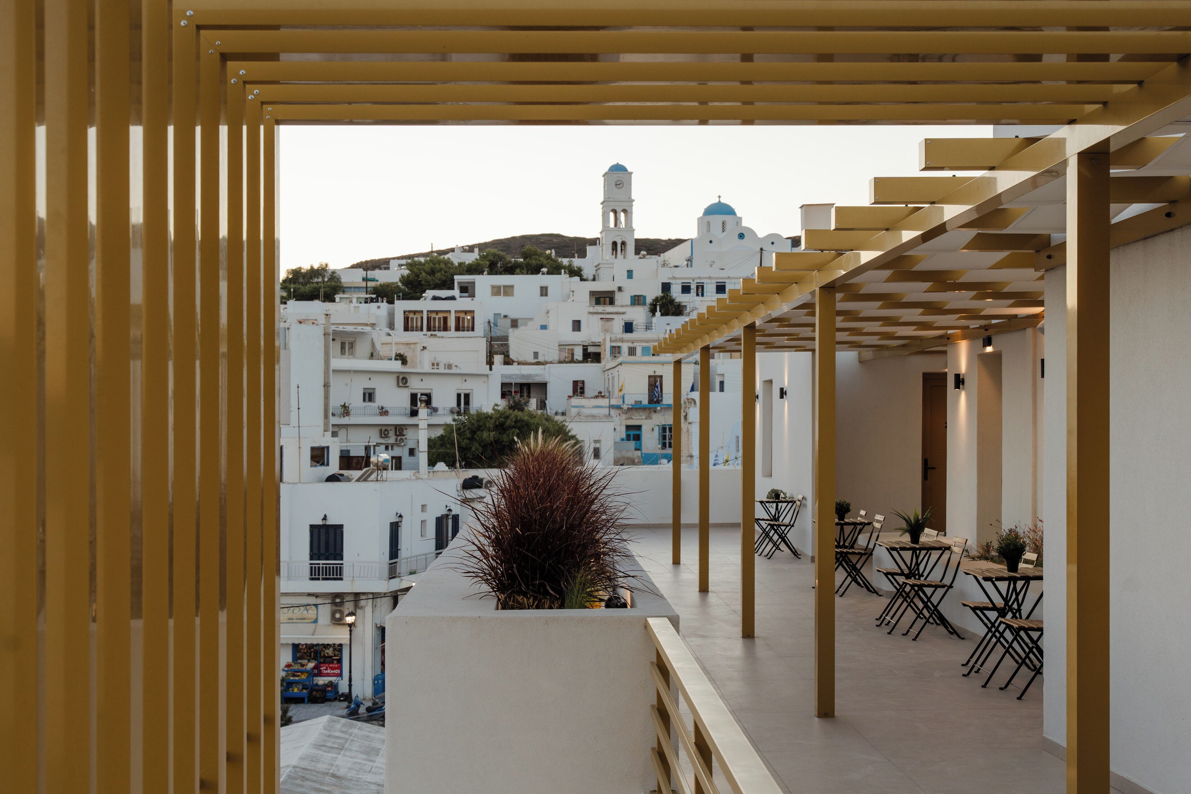 A rooftop terrace with outdoor seating and a view of white buildings with blue domes in the background.