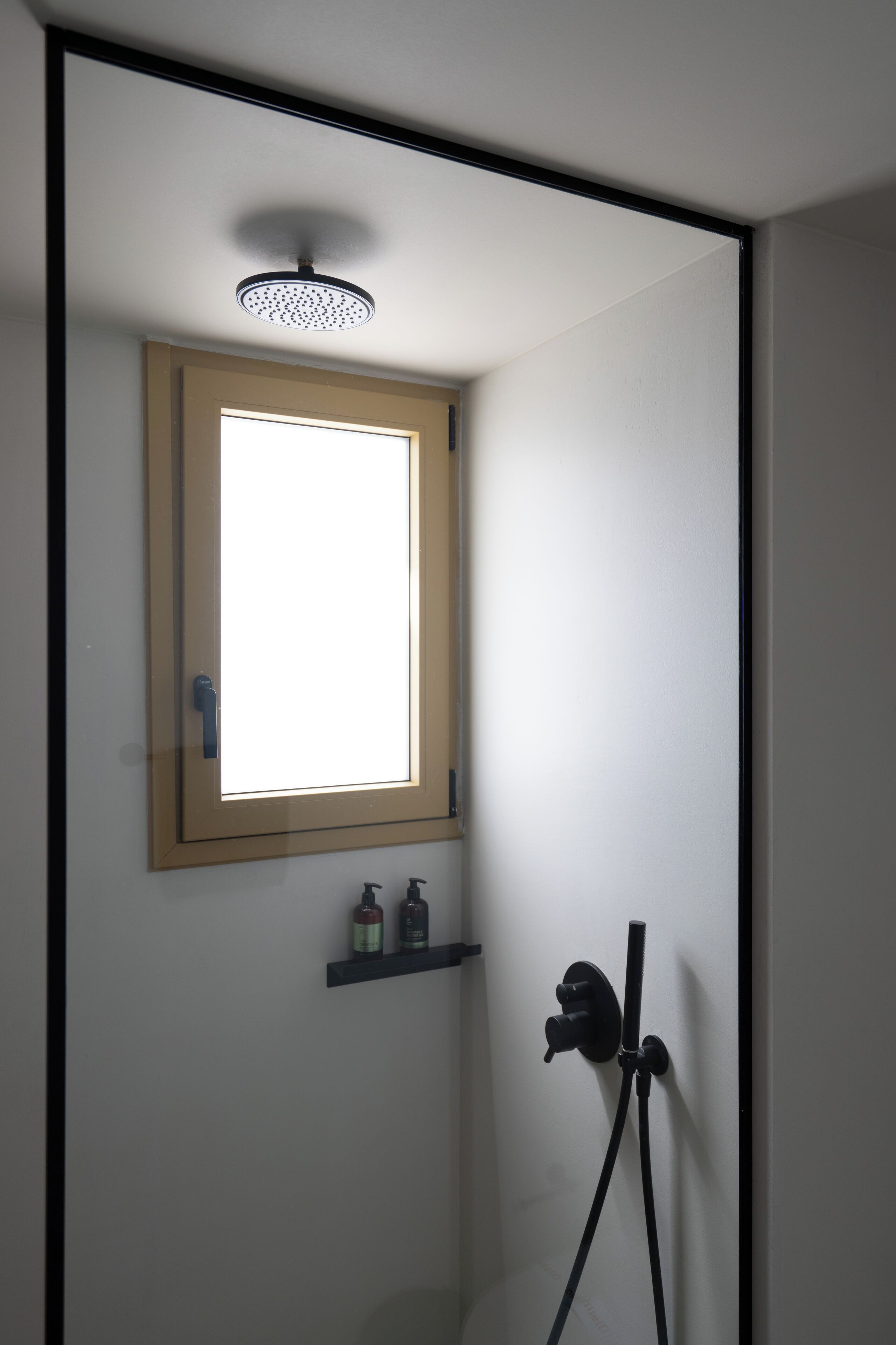 A shower area with a window, a shelf with toiletries, and a handheld showerhead.