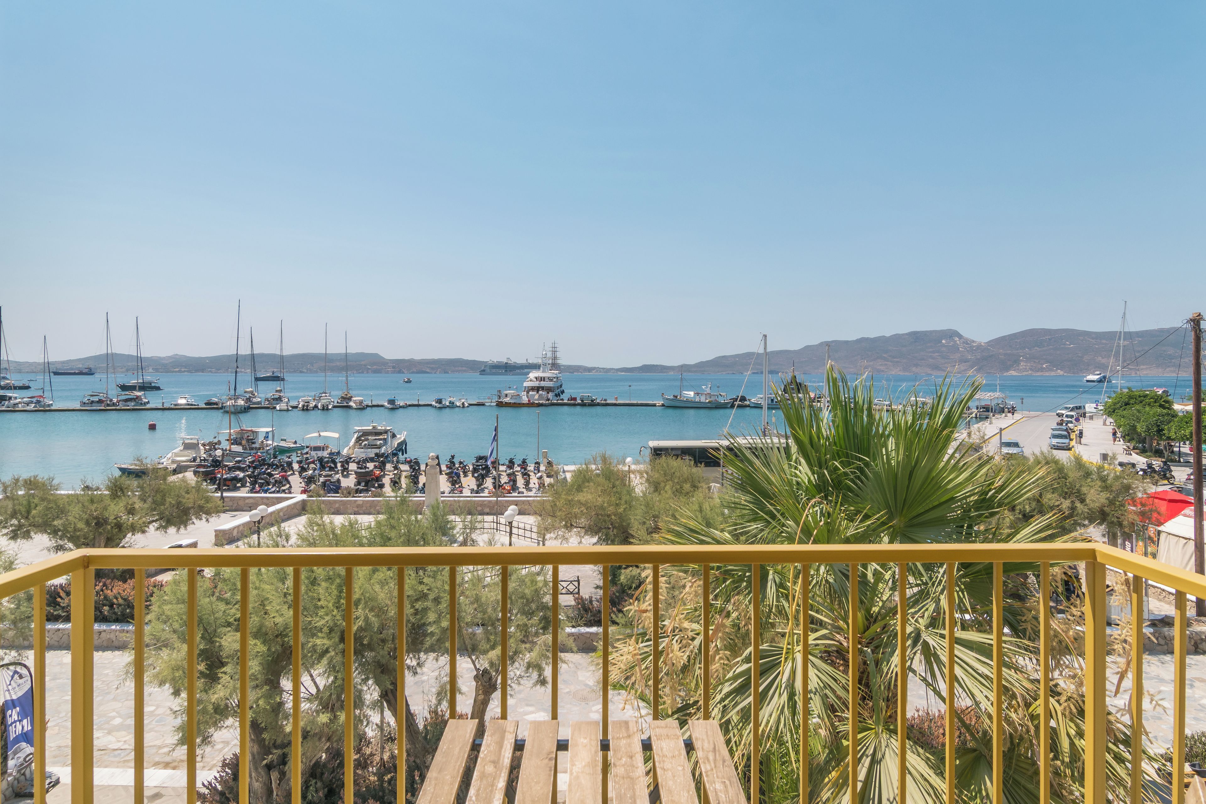 A marina with boats and yachts docked, a clear sky, and a view of the coastline.