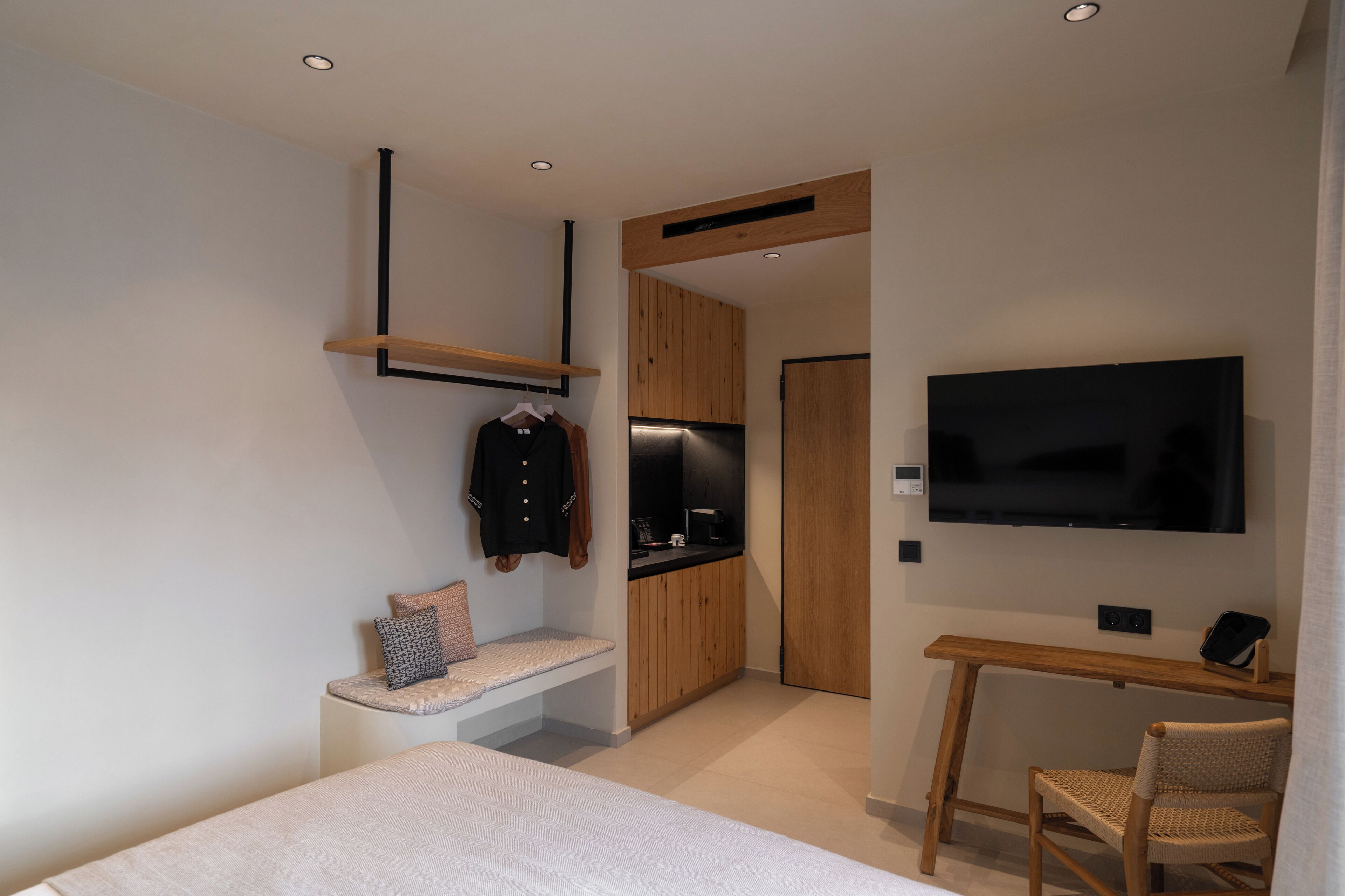 A modern hotel room with a bed, a desk, a TV, and a kitchenette.