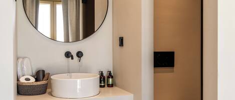 A modern bathroom with a round mirror, a white sink, and a toilet.