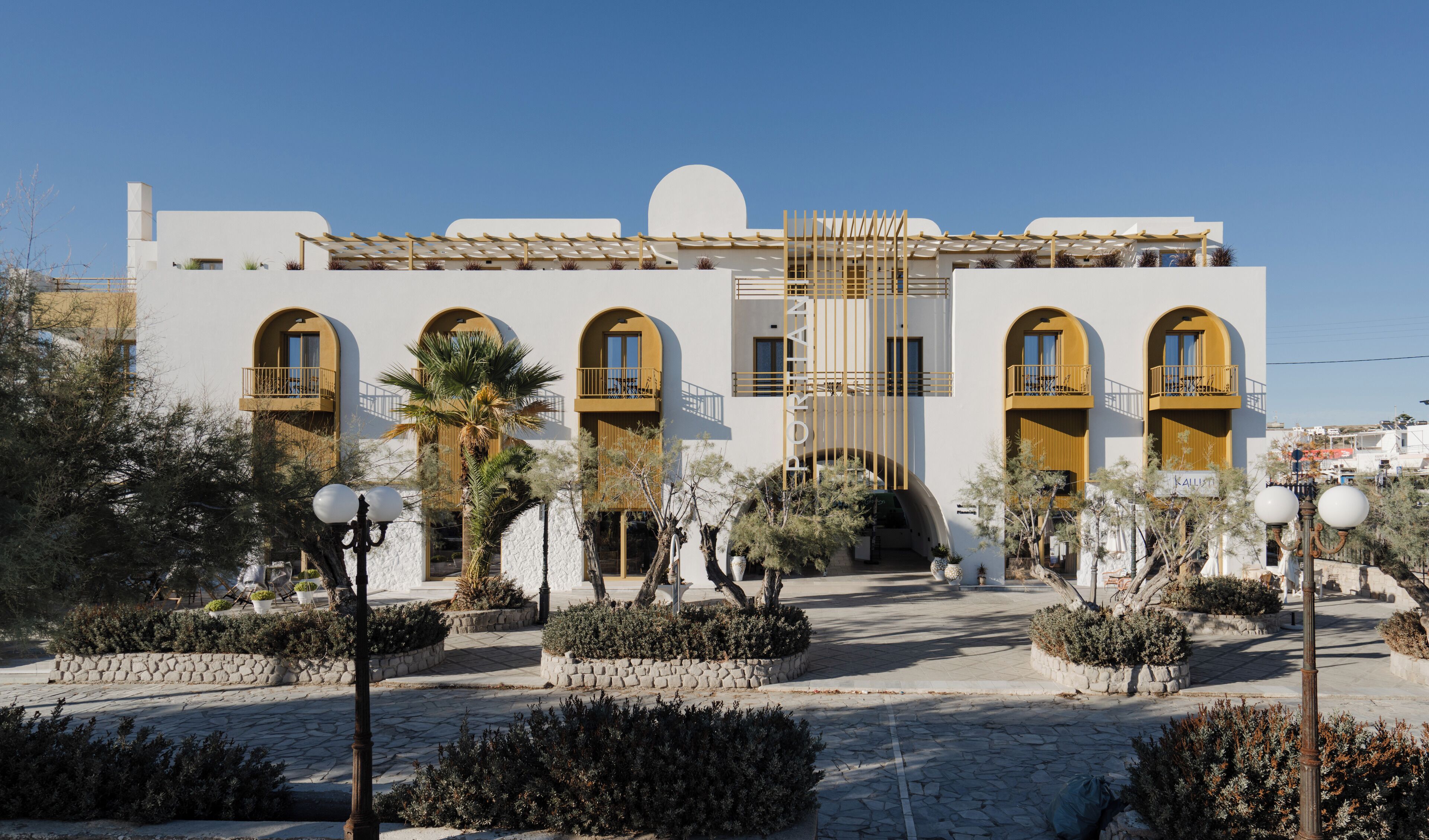 A modern building with arched windows and balconies, surrounded by landscaped gardens and stone pathways.