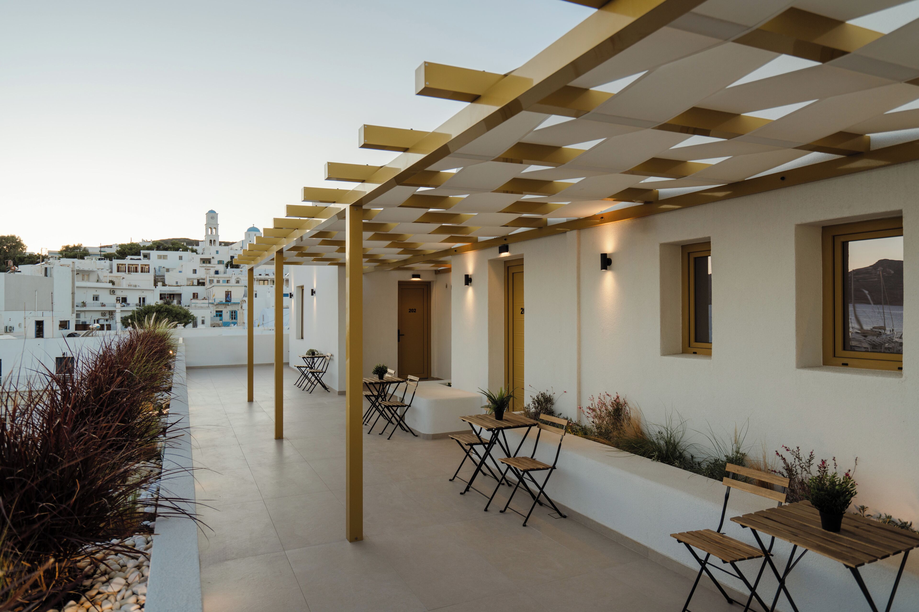 A rooftop terrace with outdoor seating, a pergola, and a view of a white building with a tower.