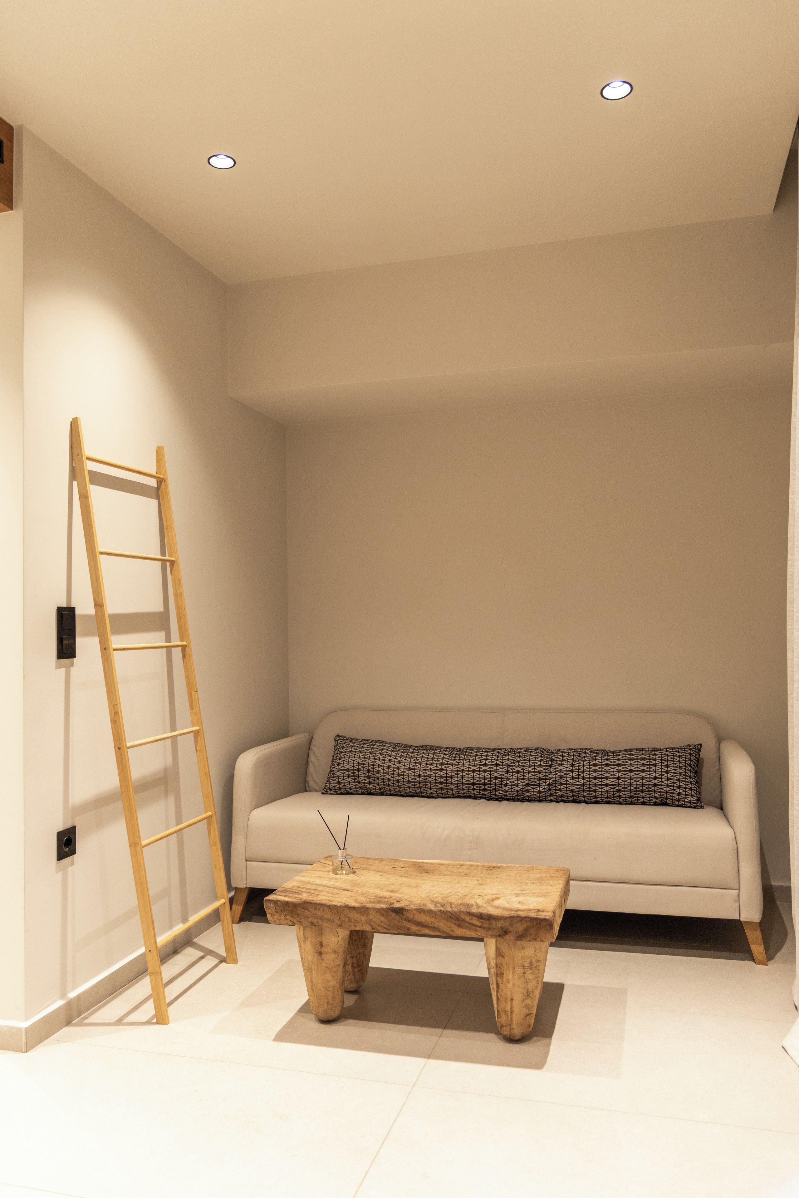 Un salón minimalista con un sofá, una mesa de centro de madera y una escalera de madera apoyada en la pared.