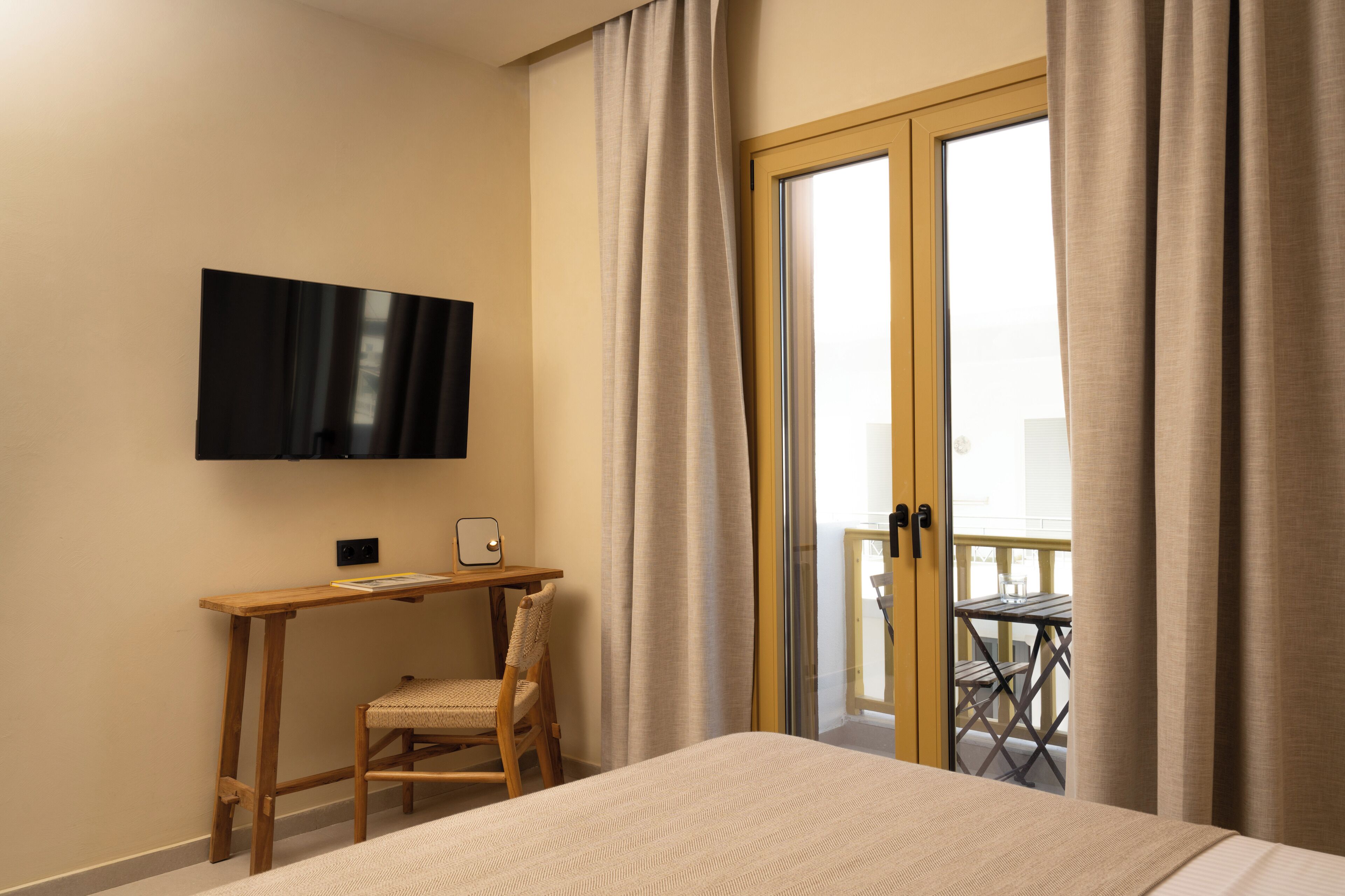 Ein Hotelzimmer mit Bett, Schreibtisch mit Stuhl, Flachbildfernseher und Balkon mit Tisch und Stühlen.