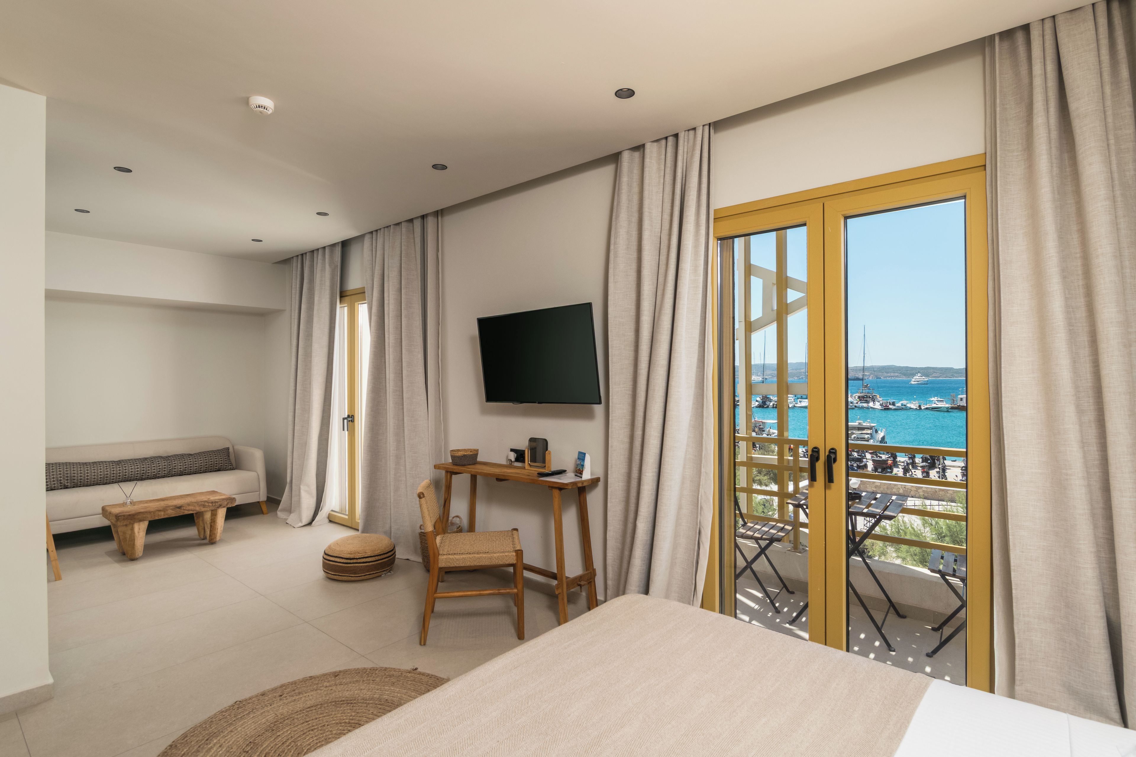 A hotel room with a bed, a TV, a sofa, a table, and a view of the sea.