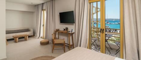 Habitación de hotel con cama, televisor, sofá, mesa y vista al mar.